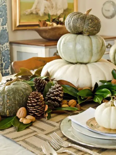 White and green pumpkins placed on magnolia leaves with pine cones and nuts make a beautiful centerpiece (HGTV)