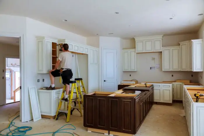 A man renovating property on a ladder in a kitchen.