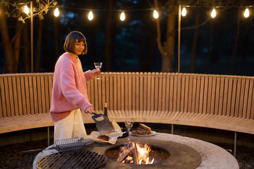 A woman in a pink sweater is sitting around a fire pit.